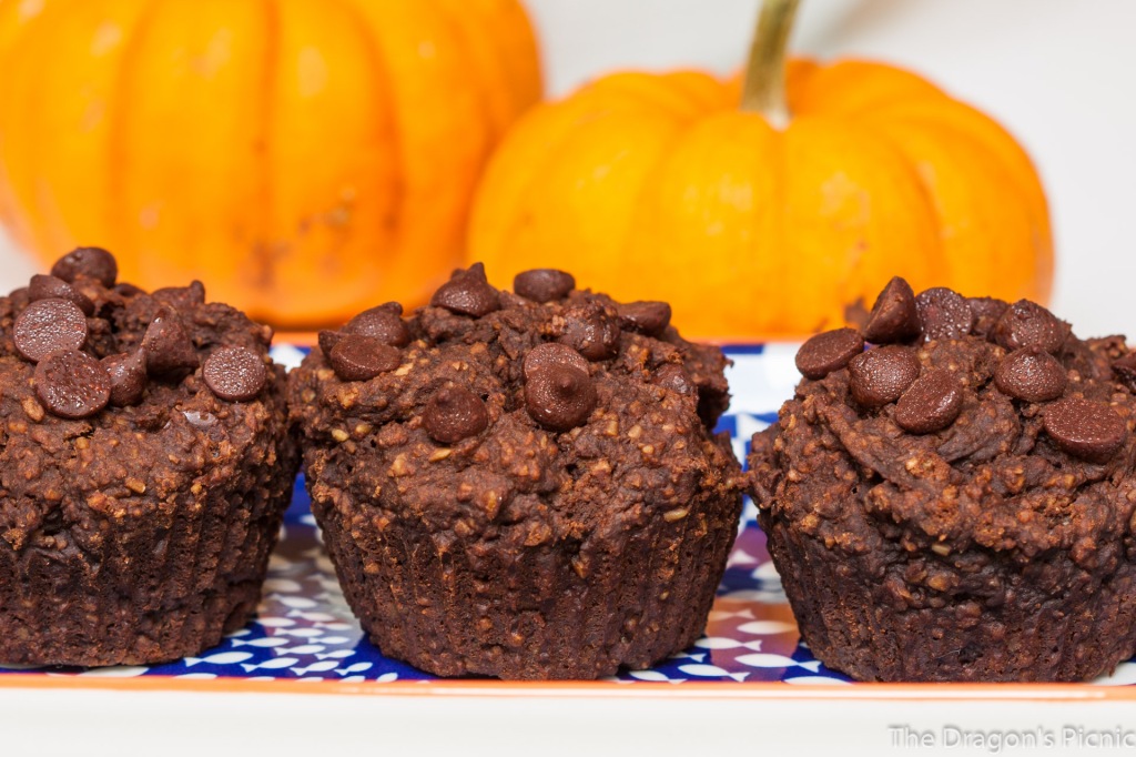 close up of three chocolate pumpkin muffins with two pumpkins in background