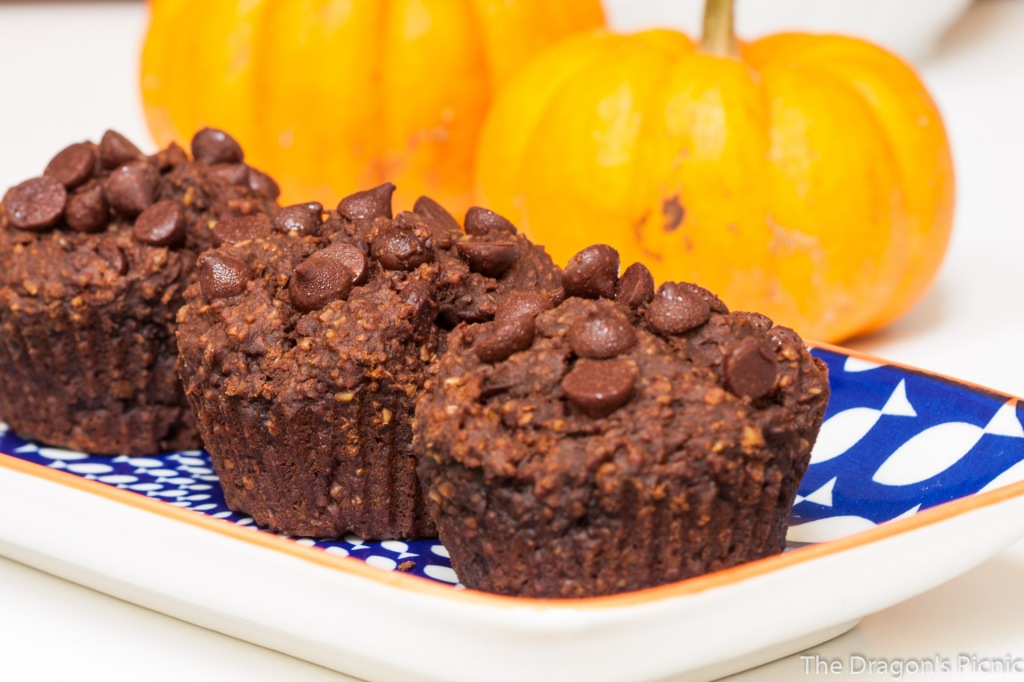 close up of three chocolate pumpkin muffins with pumpkins in the background